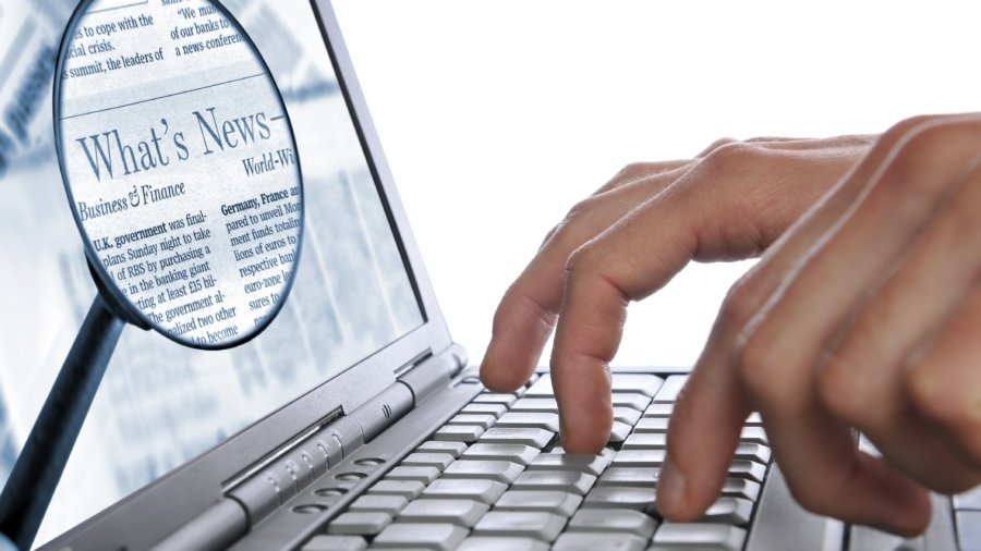 OnLine News, man’s hands laptop keyboard, magnifying glass on screen